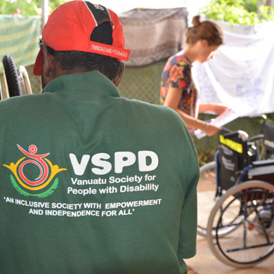 James Kalo faces away from camera with the VSPD logo showing. Motivation Australia staff member Claire is in the background examining a wheelchair