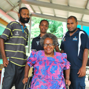 Vanuatu: A woman using a wheelchair smiles for the camera. Two men and a woman stand behind her, also smiling