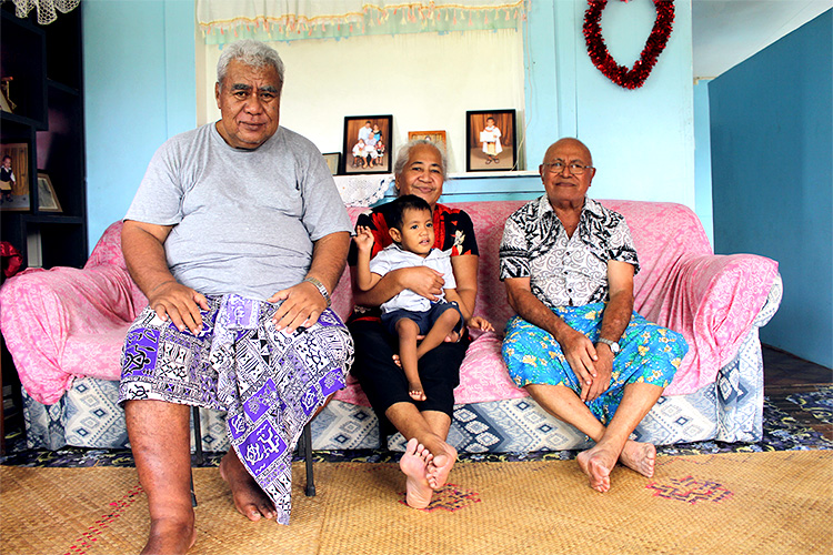 A family photo of Jedediah, his parents and his grandfather. They are sitting on a sofa inside their home and smiling at the camera.