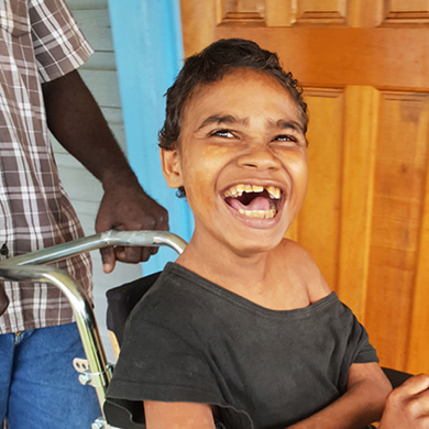 Joseph sits in his new wheelchair smiling brightly.