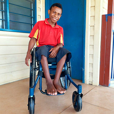 Jack sits smiling in his new wheelchair outside his school.