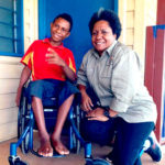 Almah and a young boy using a wheelchair pose for the camera, smiling.