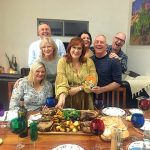 A group of people, all smiling, are gathered in front of a dinner table full of delicious food.