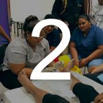 A student practices foot wound treatment on a client while a small group watches. The number 2 sits over the image.