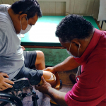 Mosese fitting a below knee prosthesis with a service user. Both are wearing masks.